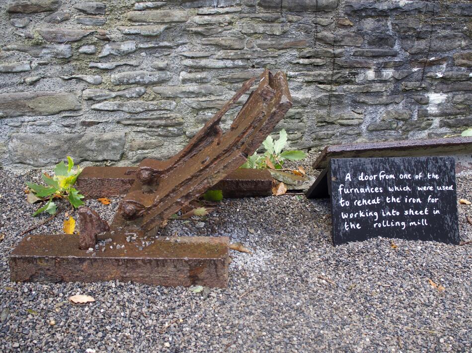 A partially rusted door mechanism next to a black sign with handwritten text.