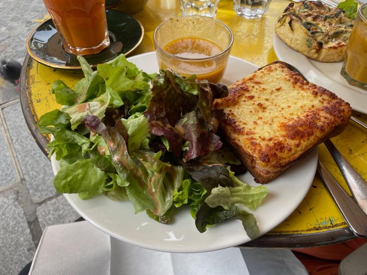 A toasted sandwich on a plate with a salad and a cup of vegetable soup.