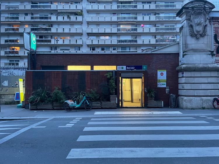 The entrance to the Bel-Air metro station. I’m standing on the opposite side of the road, looking across a pedestrian crossing into an open door on the other side. The interior of the station is lit up with a warm yellow light.